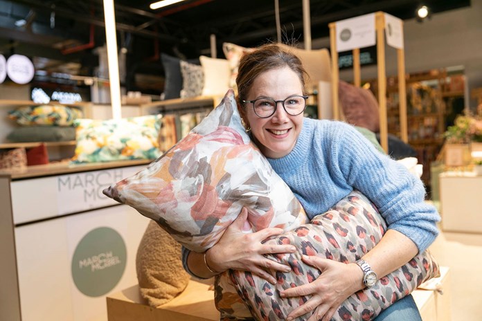 Person in a blue sweater holding two decorative pillows in a store with various home decor items displayed.