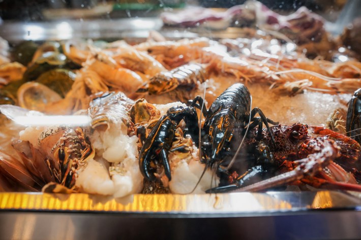 A variety of fresh seafood, including lobsters, prawns, and other shellfish, displayed on ice under a glass counter.